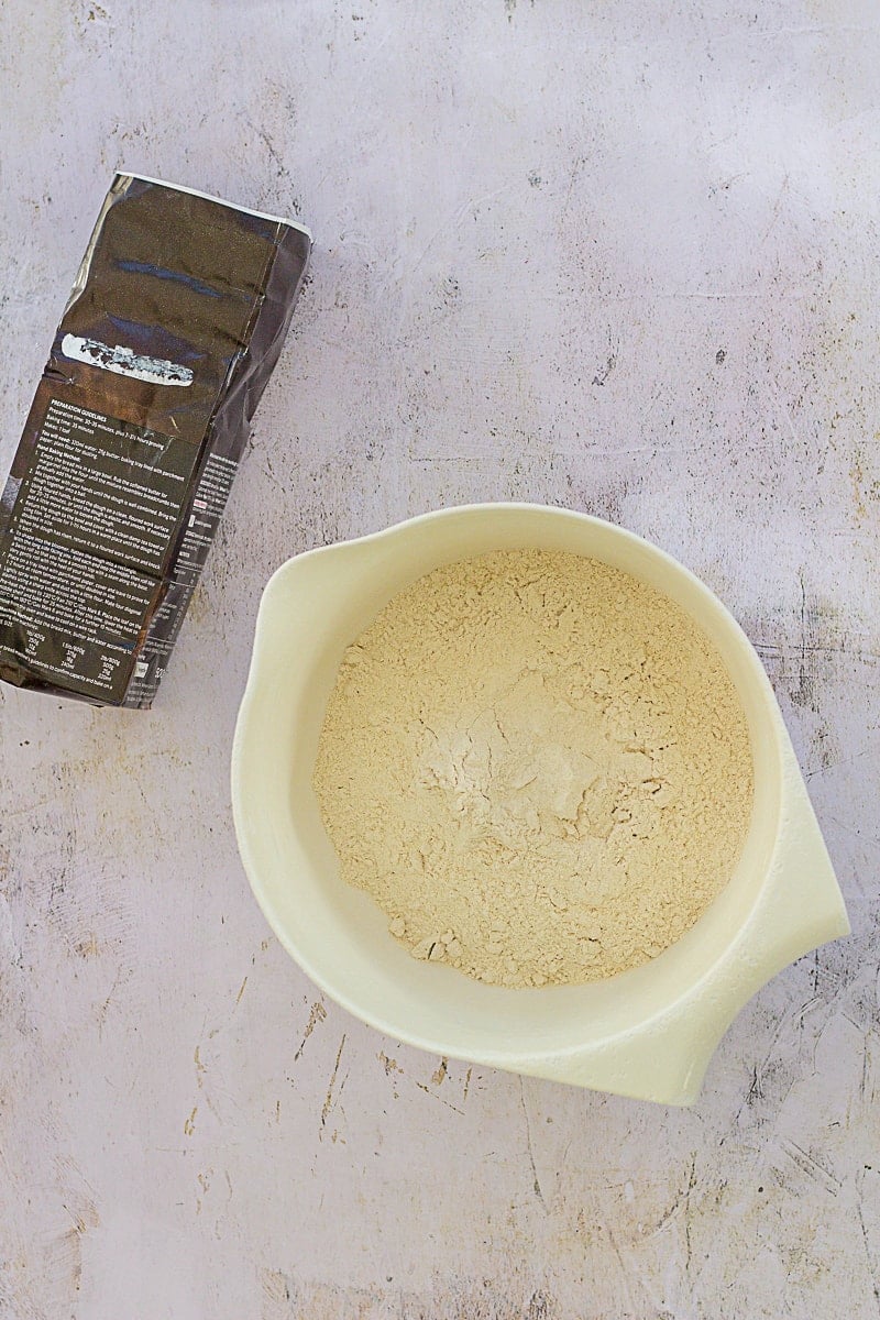 Packet bread mix in a white plastic mixing bowl with the packet lying next to it