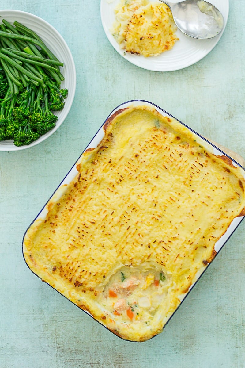 Overhead shot of Easy Peasy Fish Pie next to green vegetables.