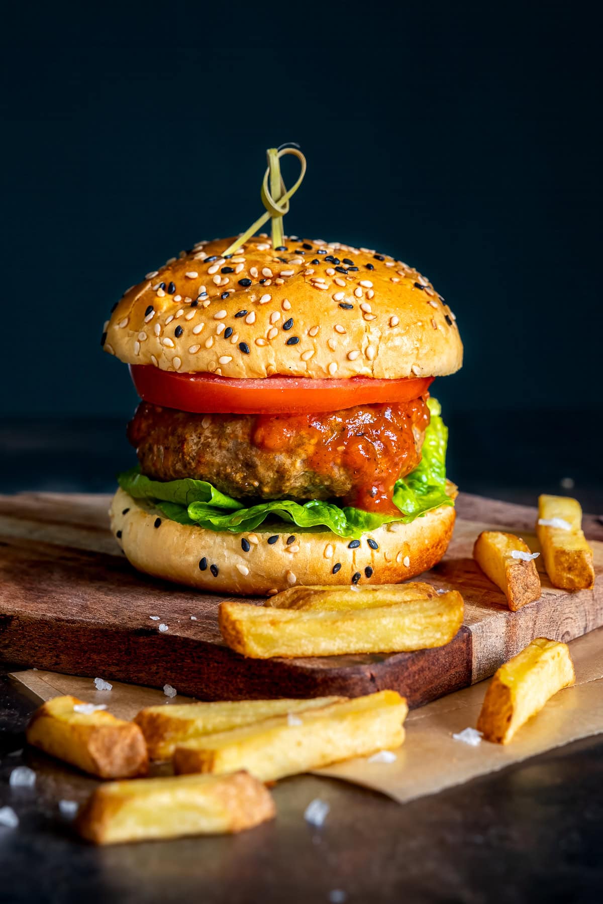 One Easy Homemade Beef Burger on a wooden board with chunky chips.