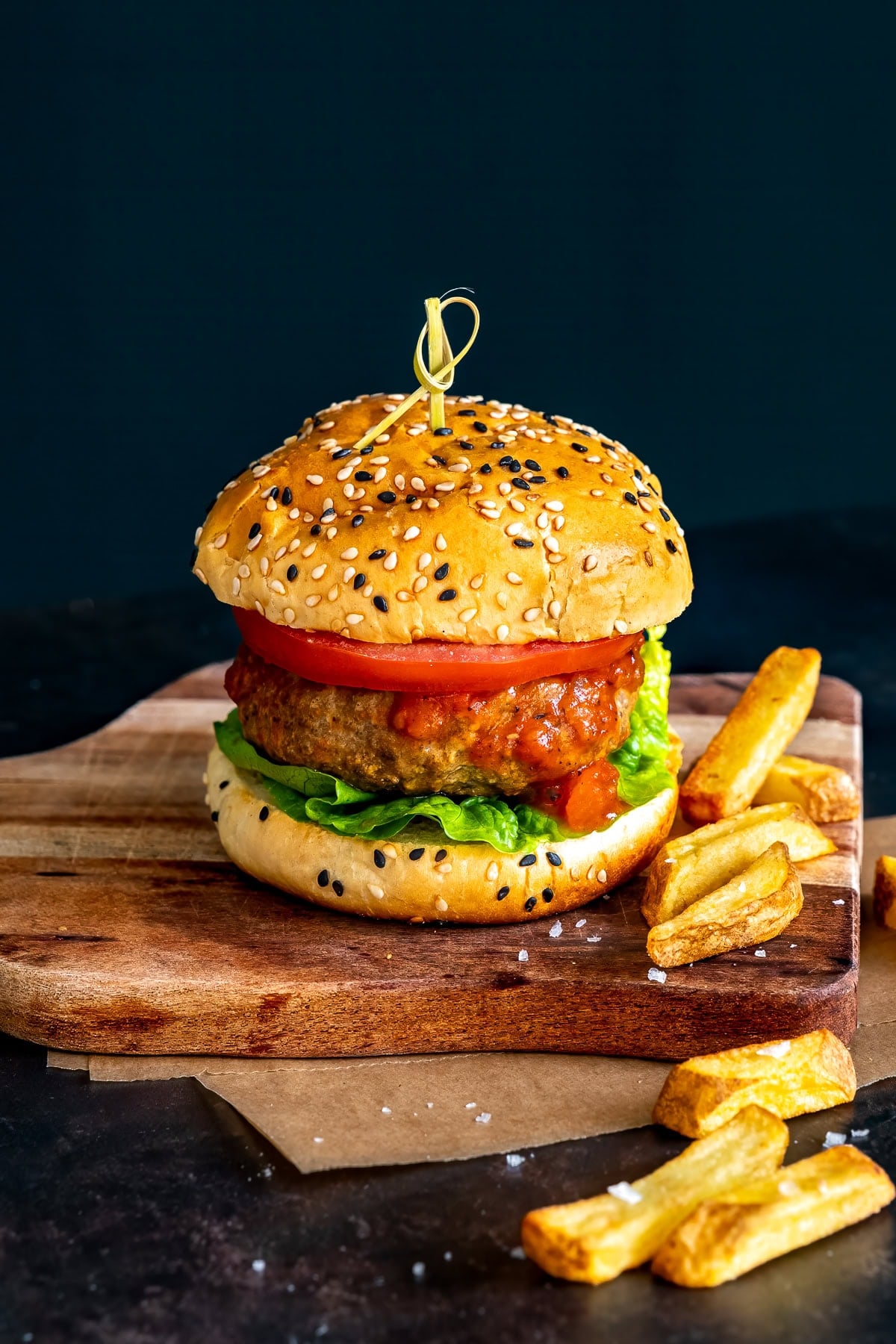 One Easy Homemade Beef Burger on a wooden board with chunky chips.