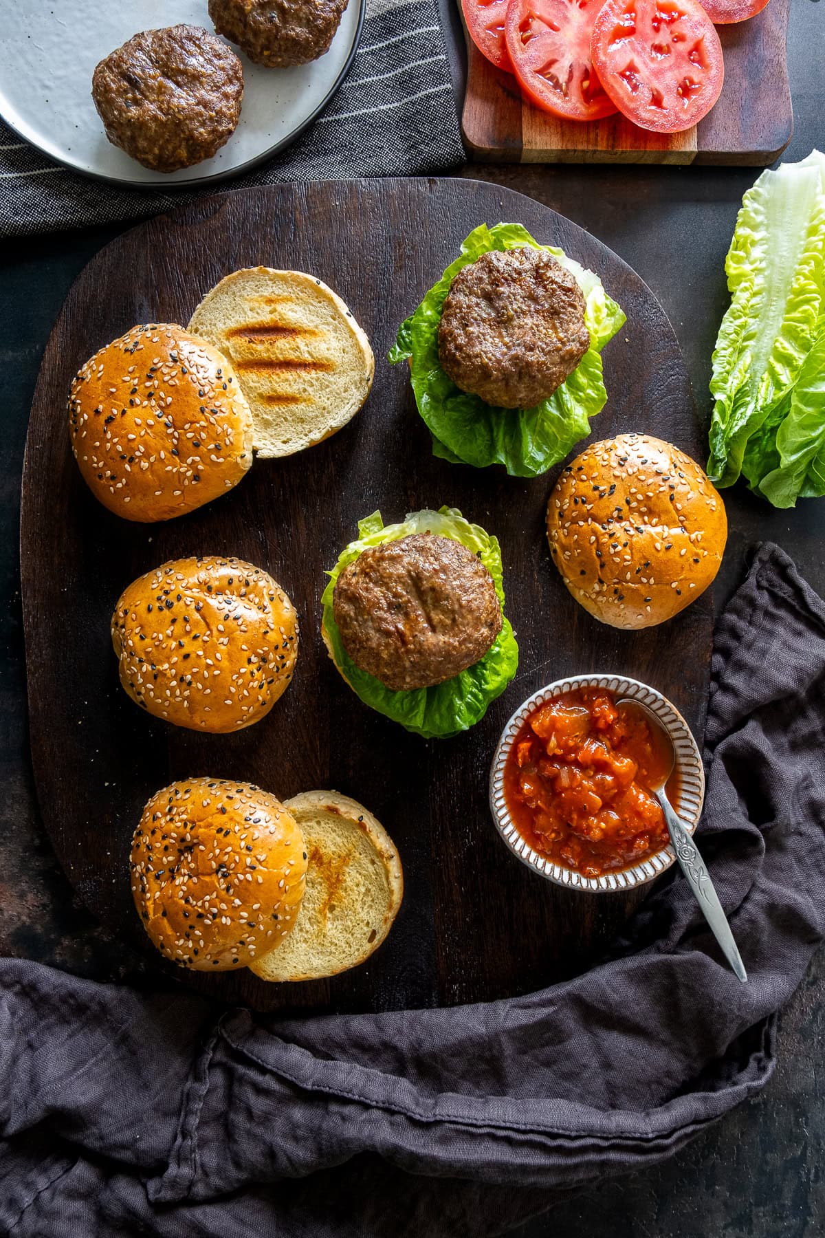 Overhead shot of Easy Homemade Beef Burgers, burger buns, lettuce, tomato slices and salsa.