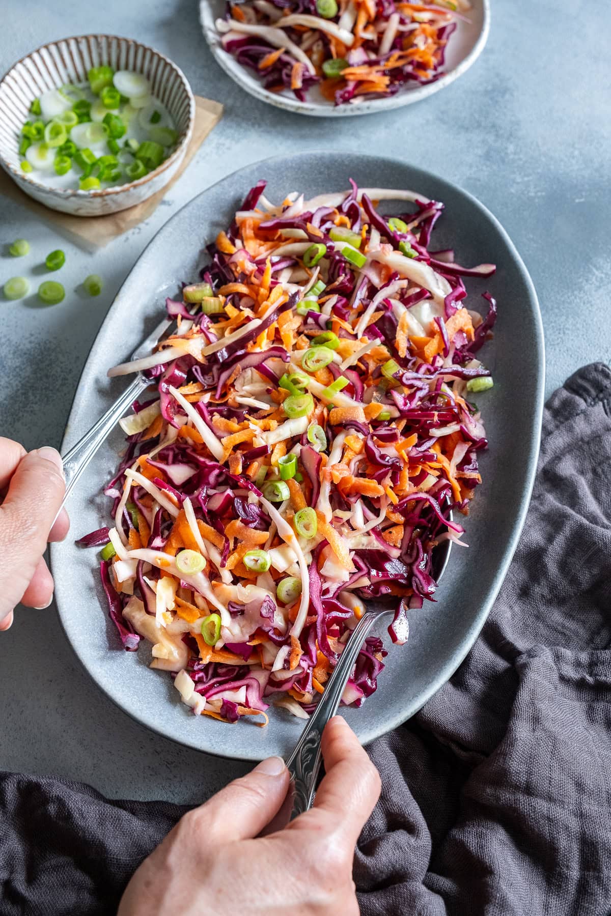 A woman's hands holding a spoon taking a portion of No Mayo, Vegan, Dairy Free, Egg Free Coleslaw.