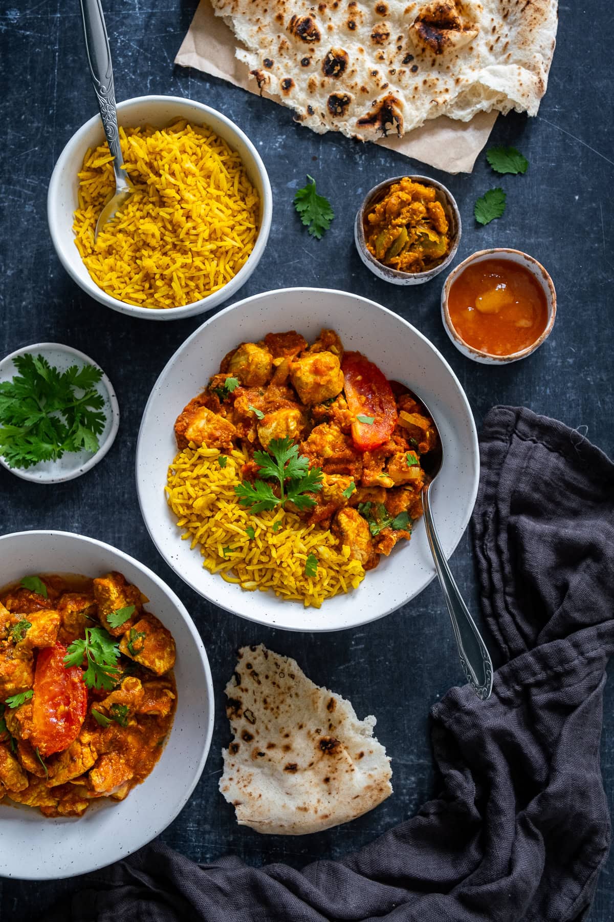 Overhead shot of Easy Chicken Rogan Josh in a bowl with Pilau Rice, Naans, Lime Pickle and Mango Chutney.