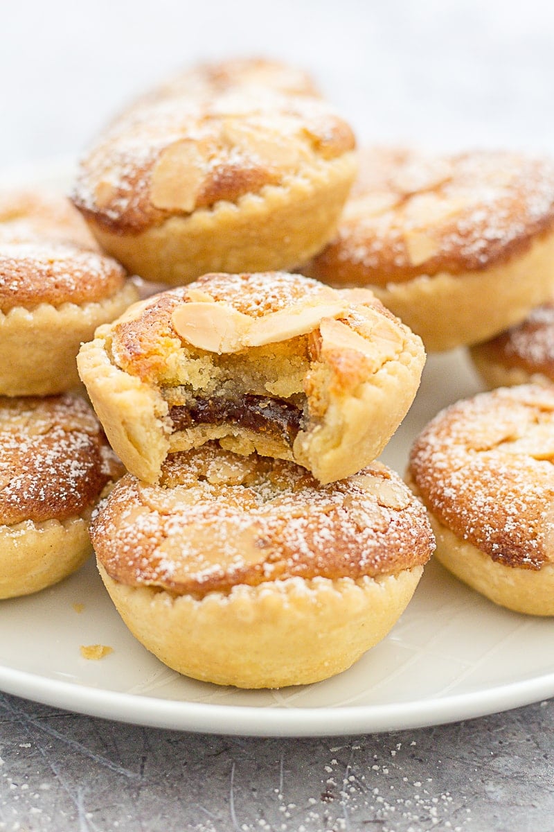 Easy Frangipane Topped Mince Pies piled onto a plate. Once of the mince pies has had a bite taken out of it.