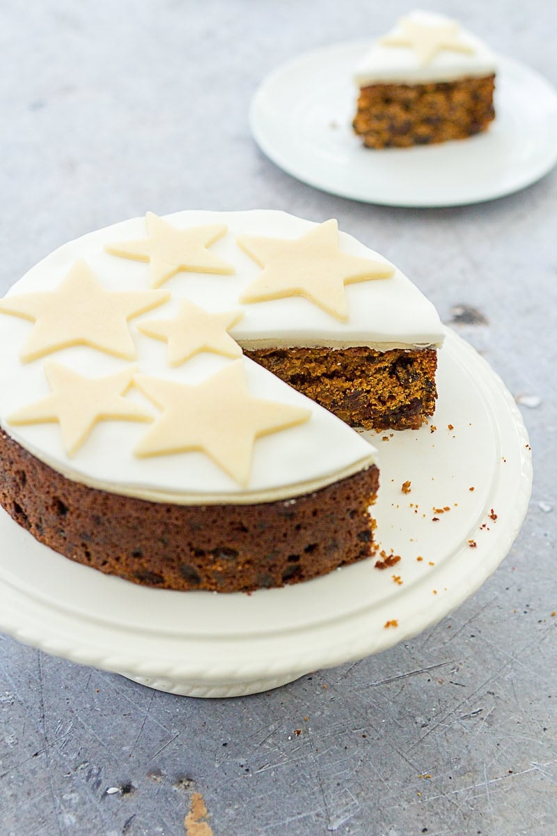 Last Minute Emergency Christmas Cake on a stand. One piece has been cut out and is on a small plate behind the cake stand.