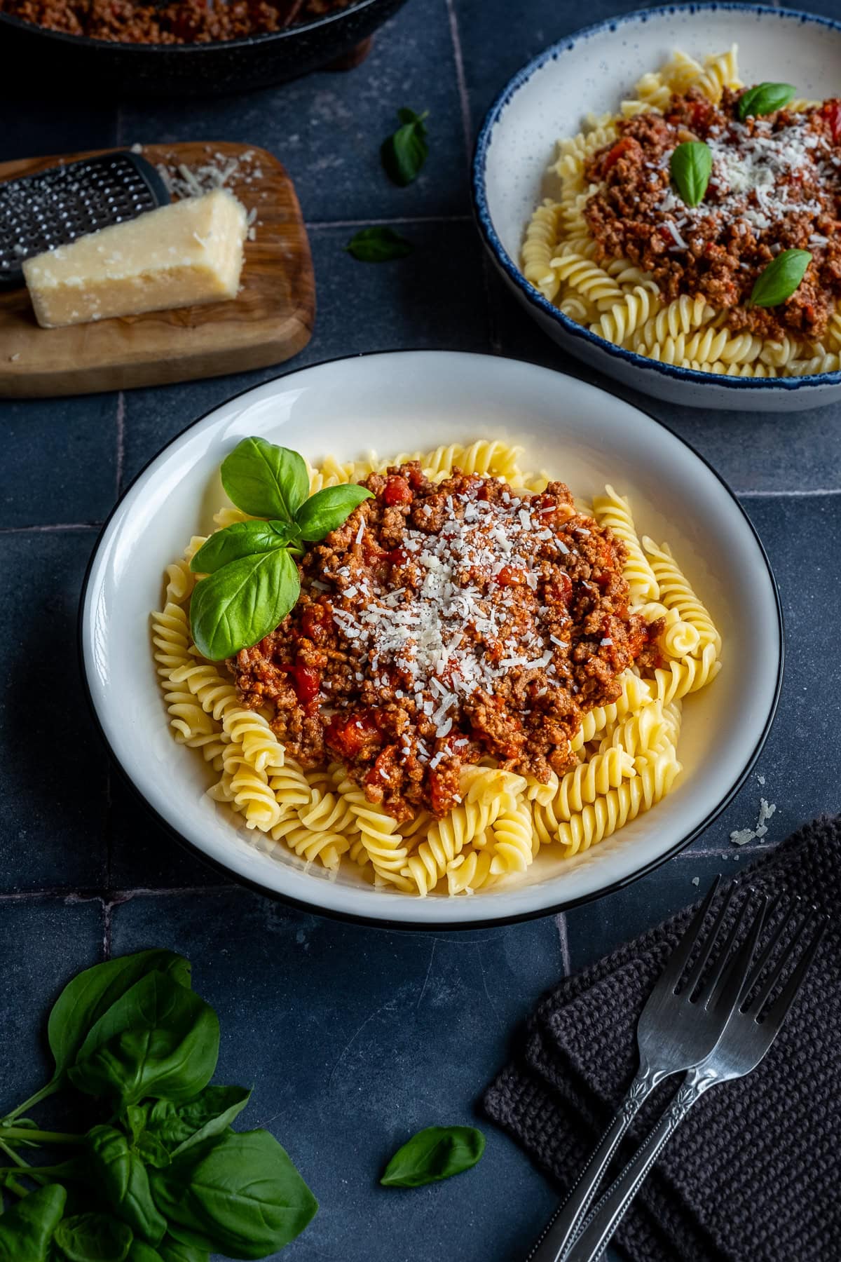 Fusilli Bolognese in a bowl with cheese and basil.