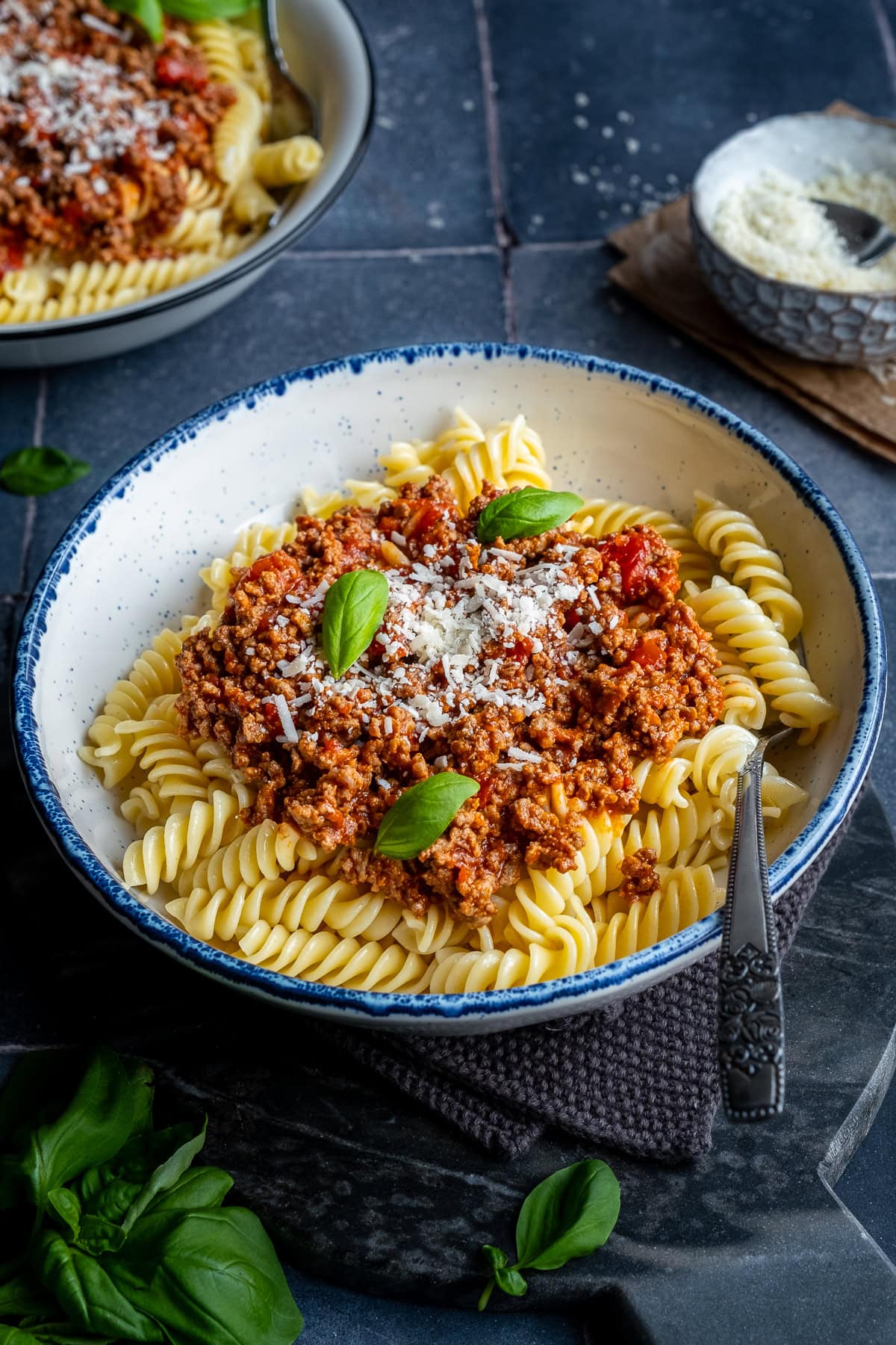 Fusilli Bolognese in a bowl with cheese and basil.