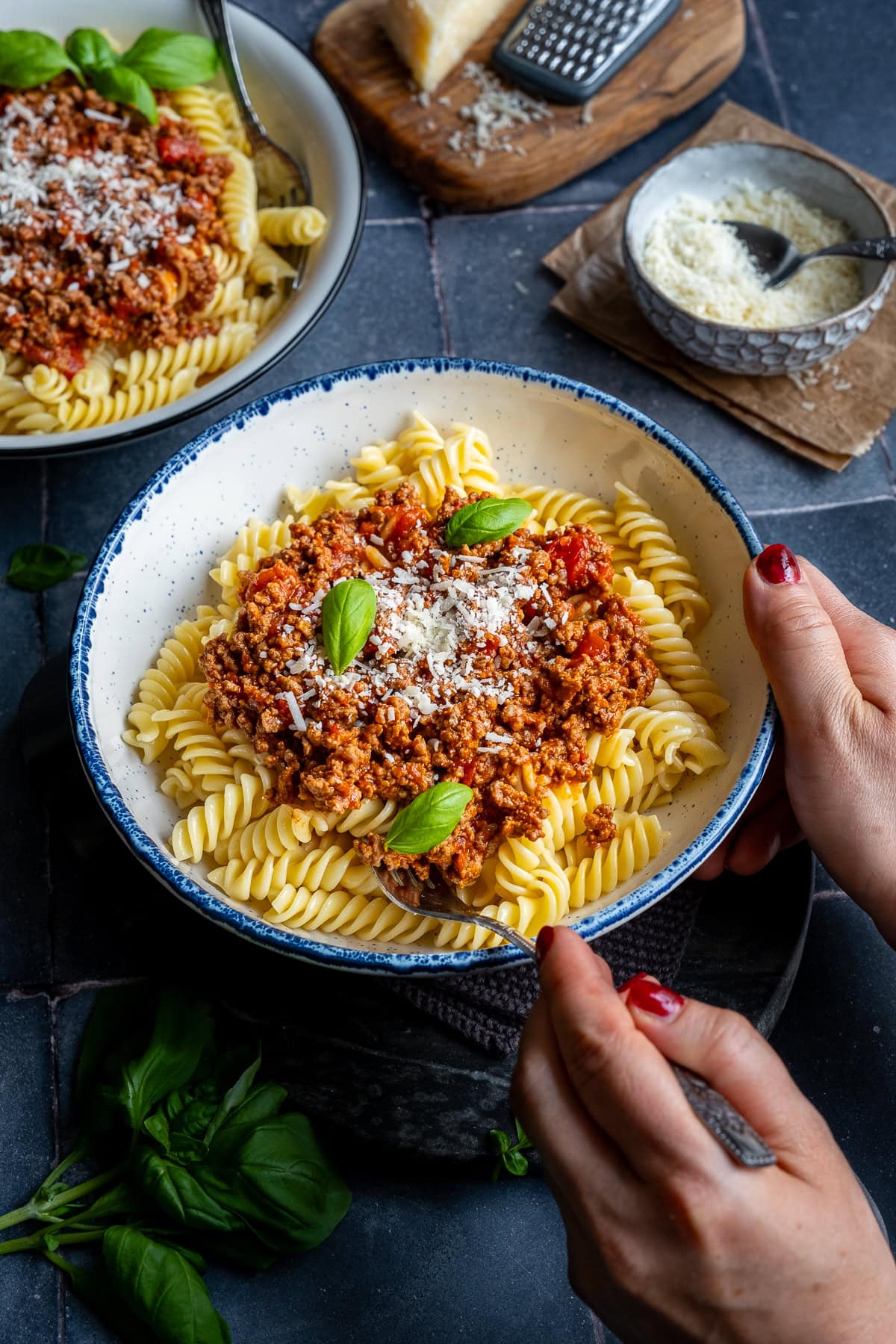 Fusilli Bolognese in a bowl. A woman's hand is holding a fork, about to take a forkful.