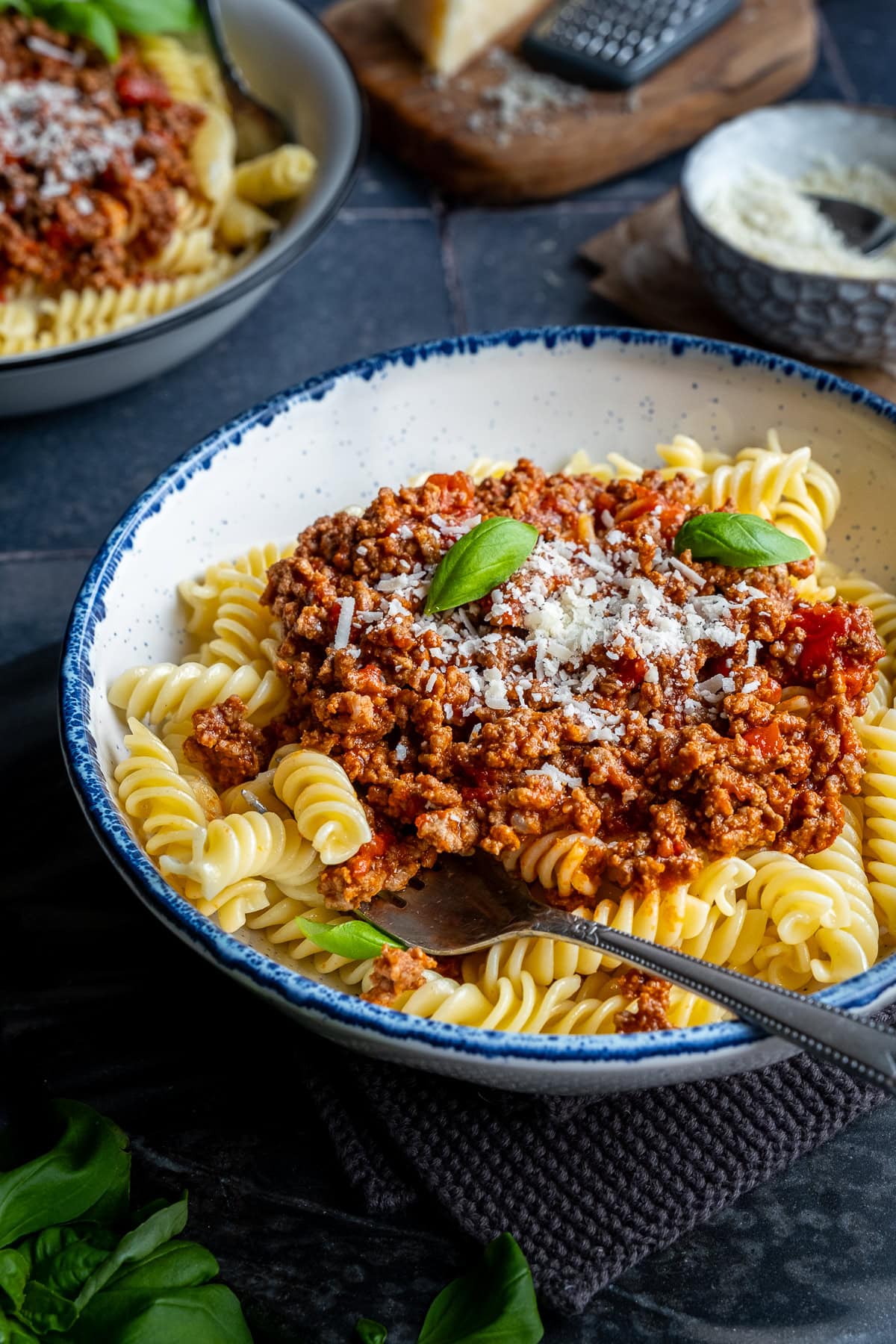 Closeup of Fusilli Bolognese in a bowl, topped with parmesan and basil.