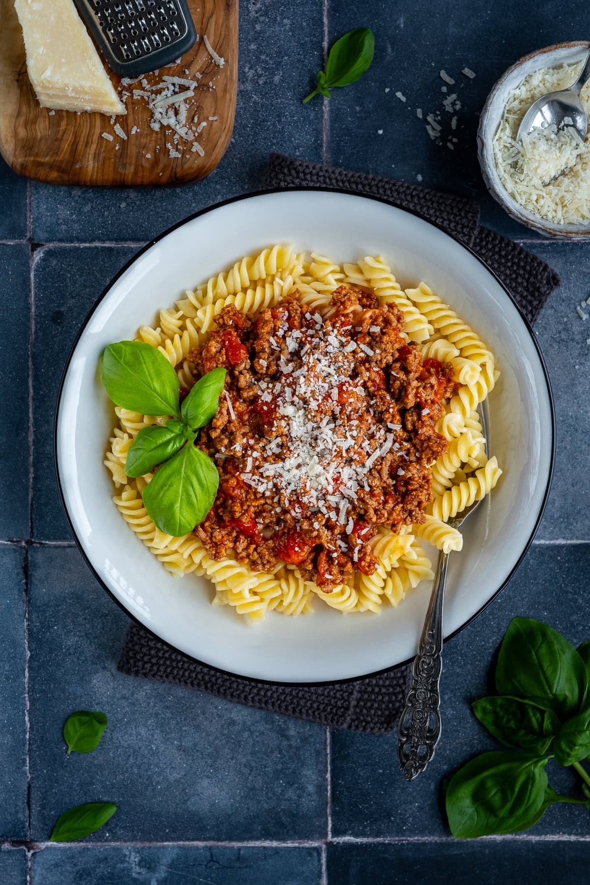 Overhead shot of 1 bowl of Fusilli Bolognese, topped with parmesan and basil.