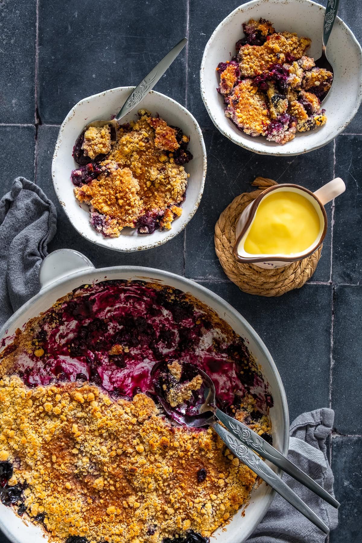 Oveahead shot of two bowls of Easy Blueberry Crumble and a jug of custard.