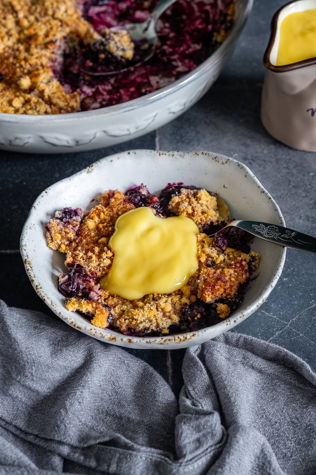 Closeup of Easy Blueberry Crumble in a bowl with custard on top.