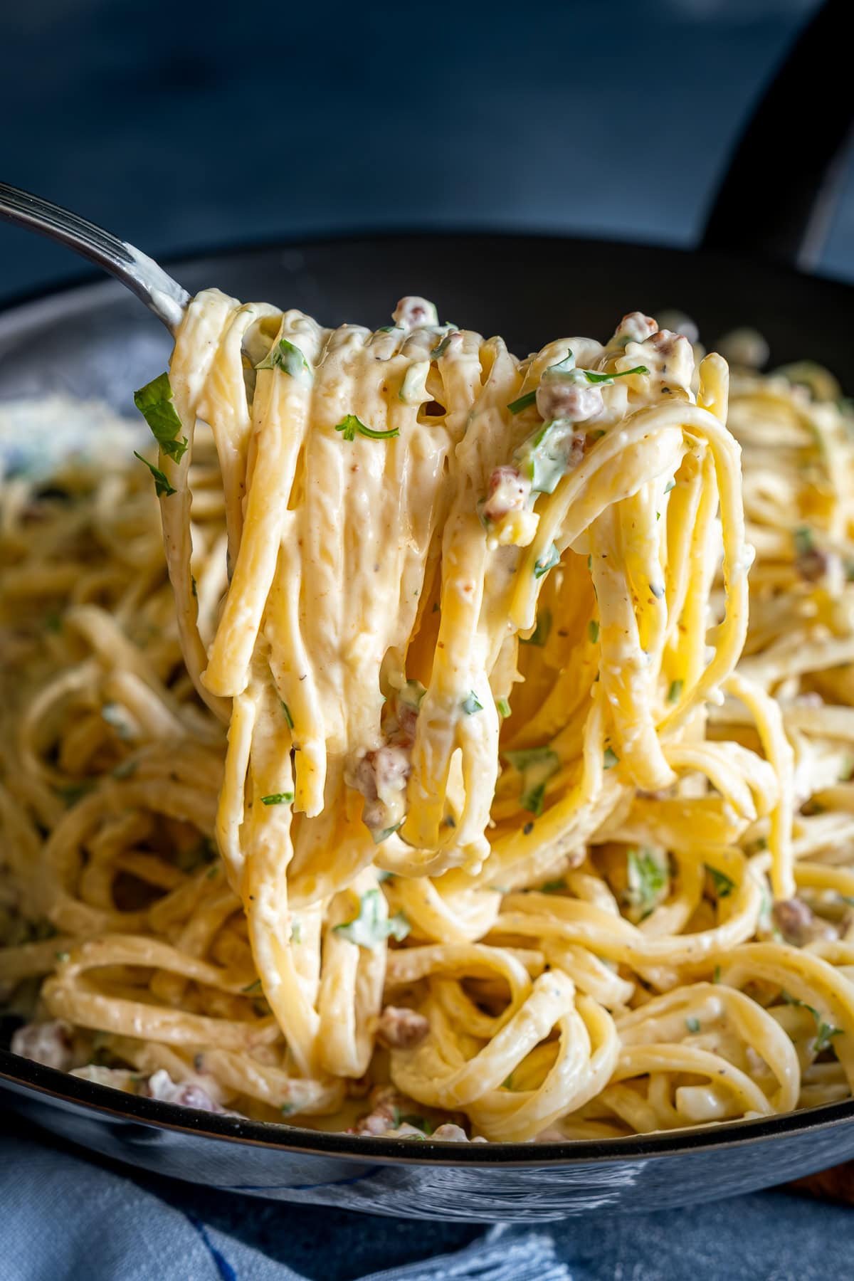 A forkful of Easy Creamy Carbonara being held up to the camera to show how creamy it is.