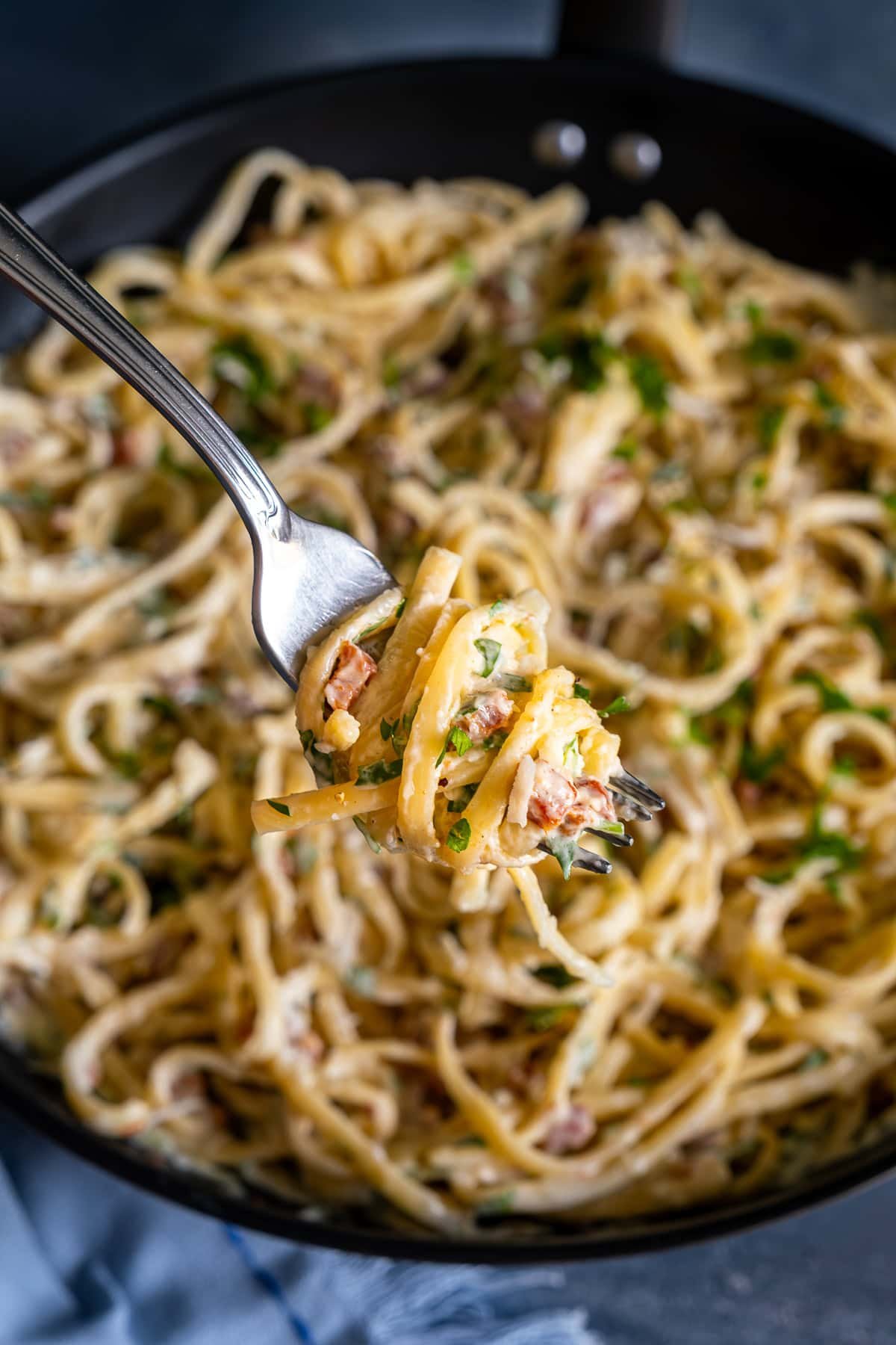 A forkful of Easy Creamy Carbonara being held up to the camera to show how creamy it is.
