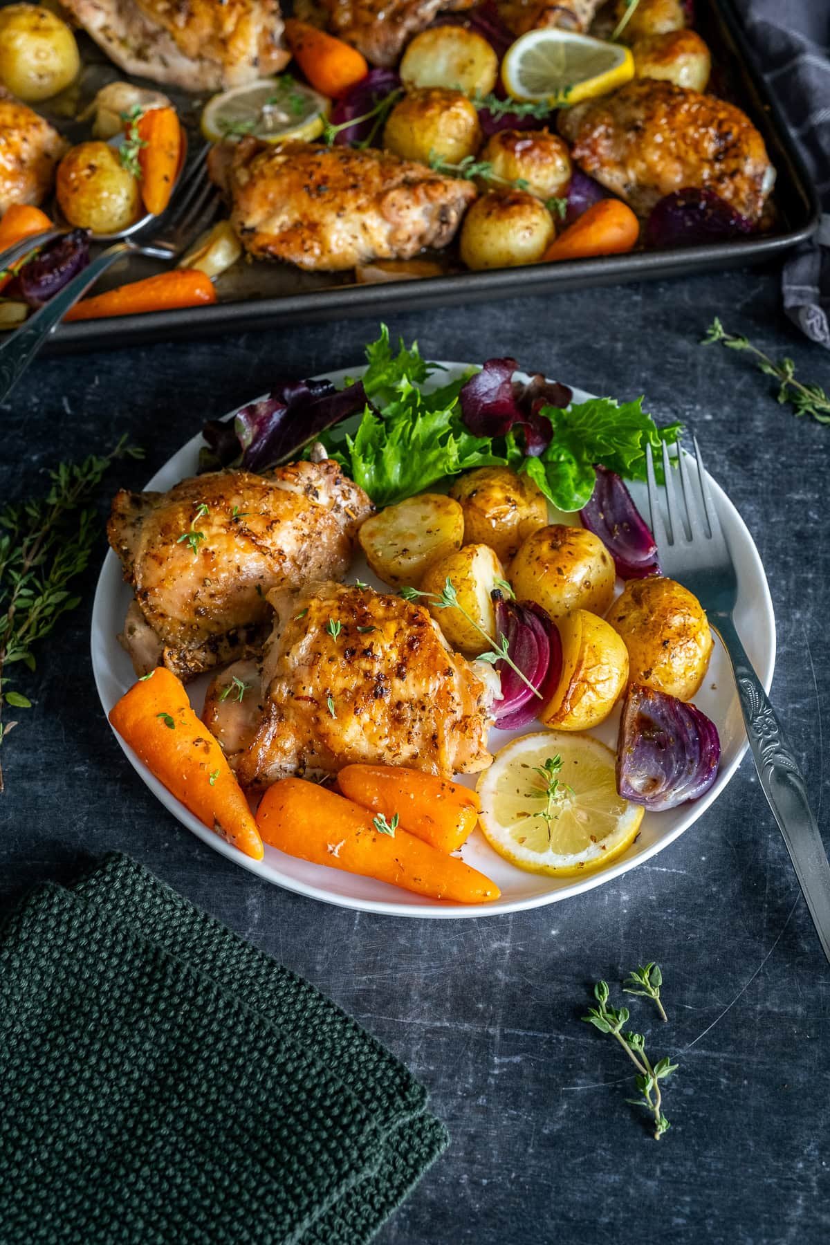Closeup of Chicken and Potato Traybake with Lemon and Garlic on a plate, with the tray in the background.