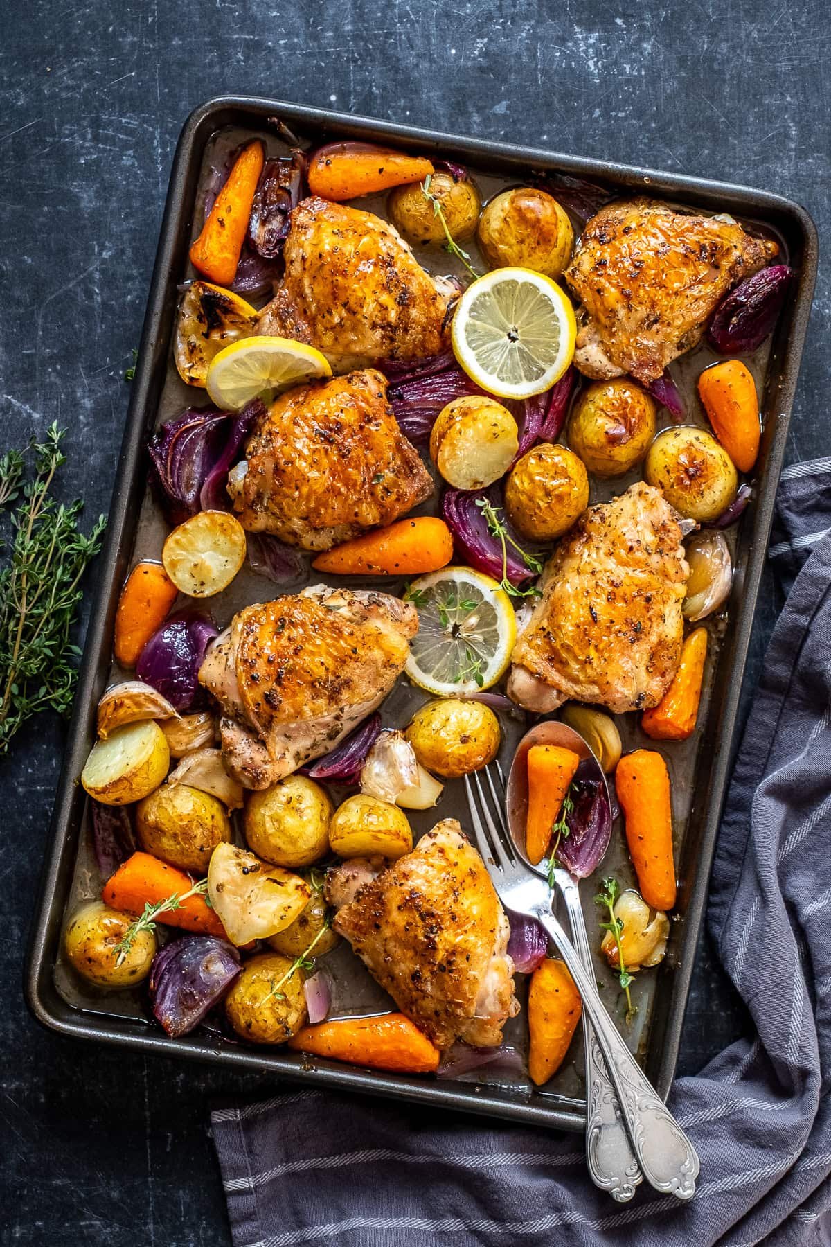 Overhead shot of Chicken and Potato Traybake on the tray with serving spoons.