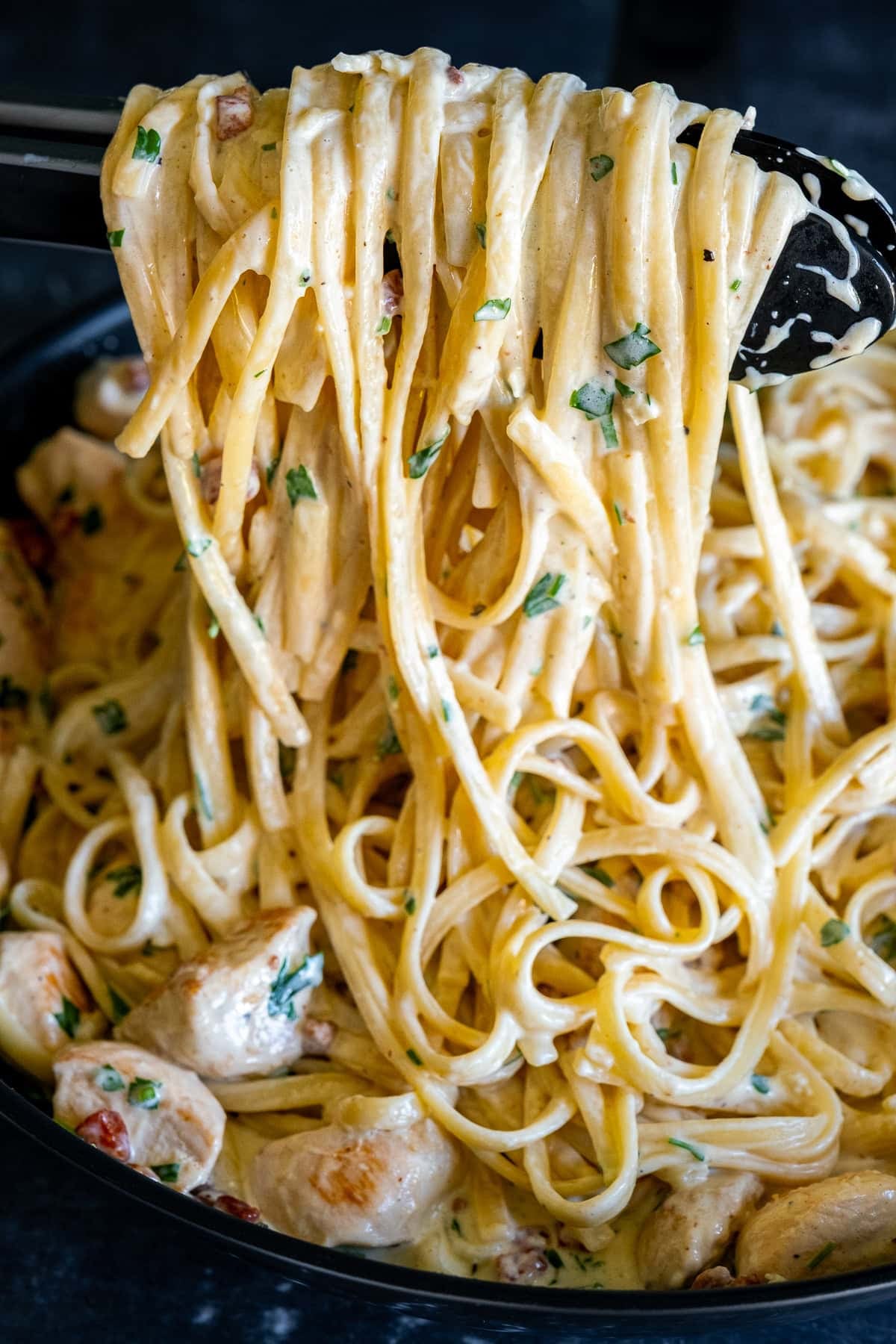 Creamy Chicken Carbonara with Bacon being held up with tongs to show how creamy it is.