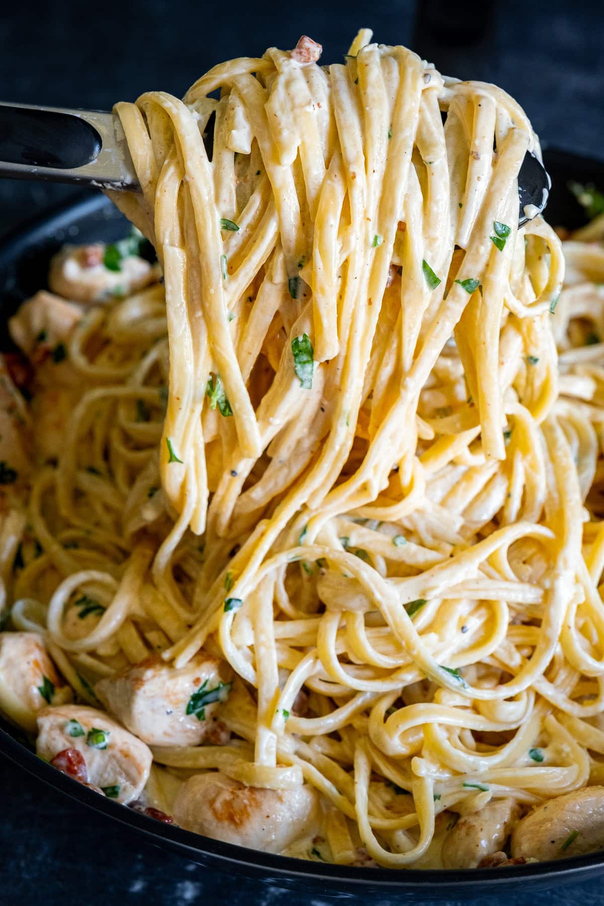 Creamy Chicken Carbonara with Bacon being held up with tongs to show how creamy it is.
