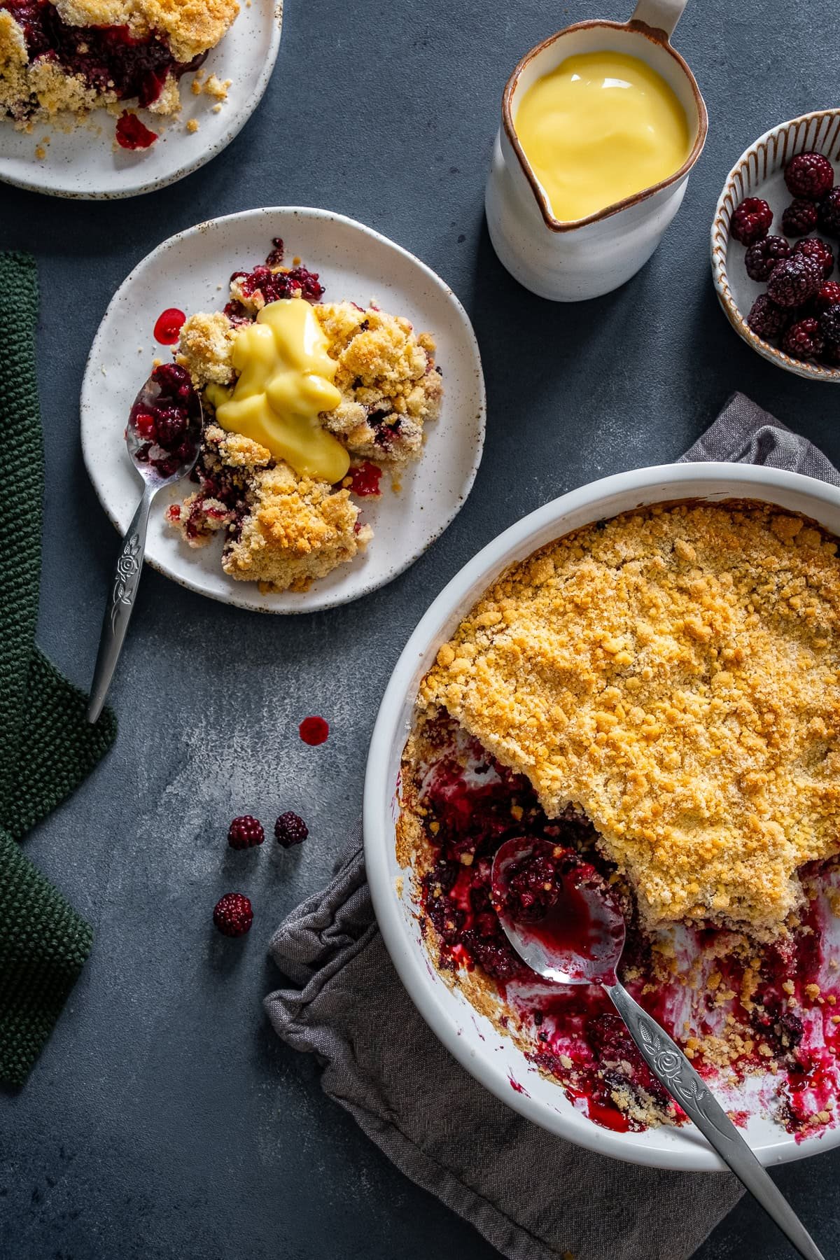 Overhead shot of Easy Blackberry Crumble in the dish and 1 plate of Easy Blackberry Crumble with custard.