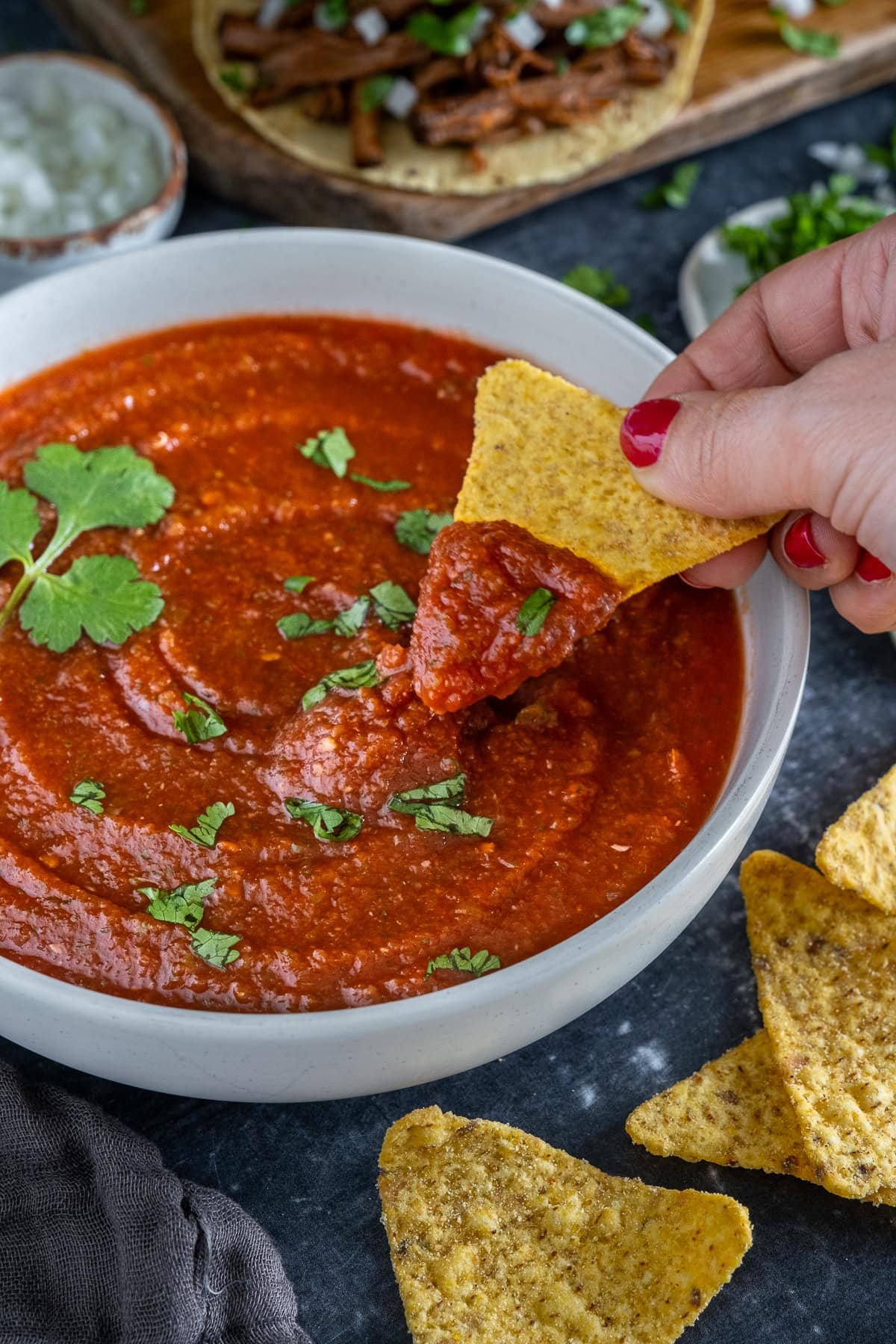 Closeup of 5 Minute Blender Salsa in a bowl, one tortilla chip has just been dipped in the salsa.