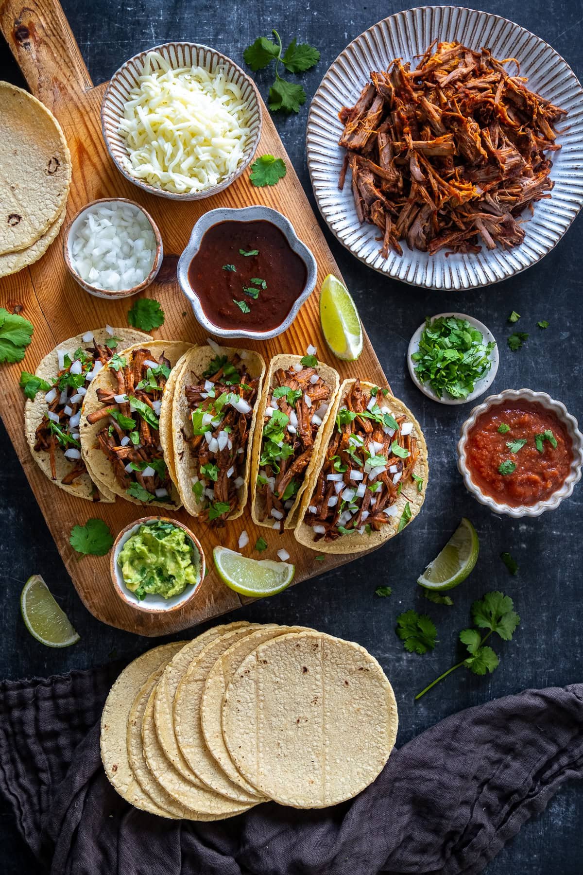 Overhead shot of Easy Beef Birria Tacos, corn tortillas, guacamole, salsa, grated cheese and sour cream.
