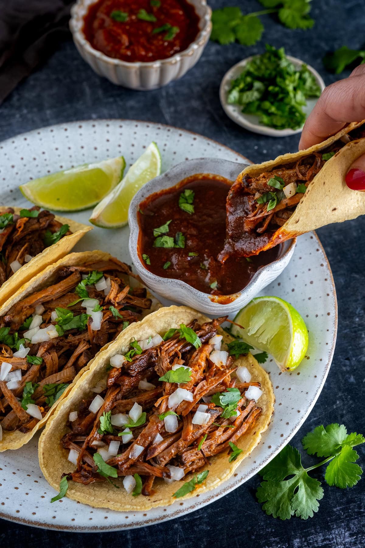 3 Beef Birria Tacos on a plate, 1 taco being dipped into birria consome