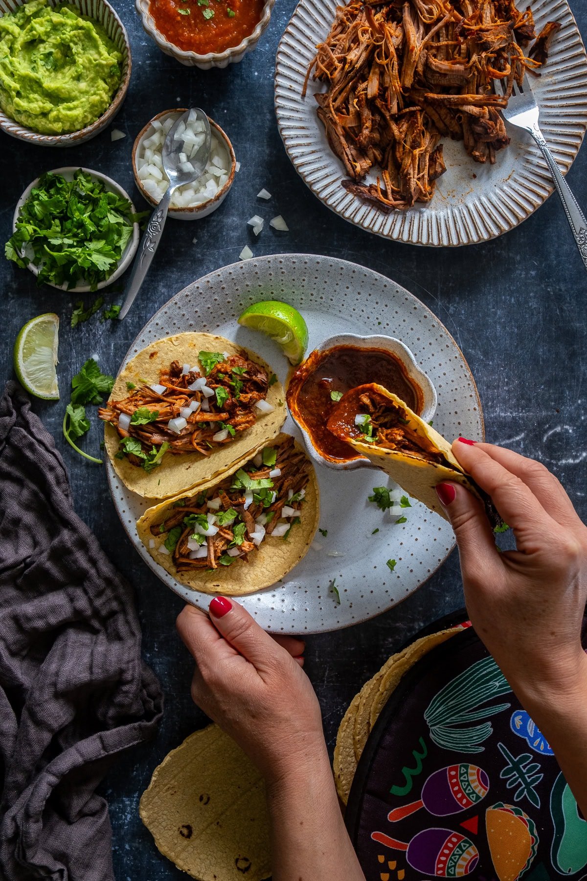Overhead shot of 3 Easy Beef Birria Tacos on a plate with a small bowl of consome. One of the tacos is being dipped in the consome.