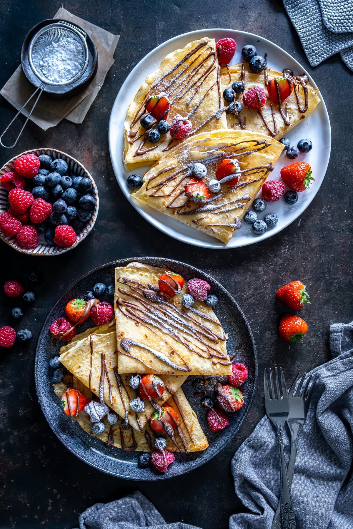 Two plates of crepes topped with berries and nutella.