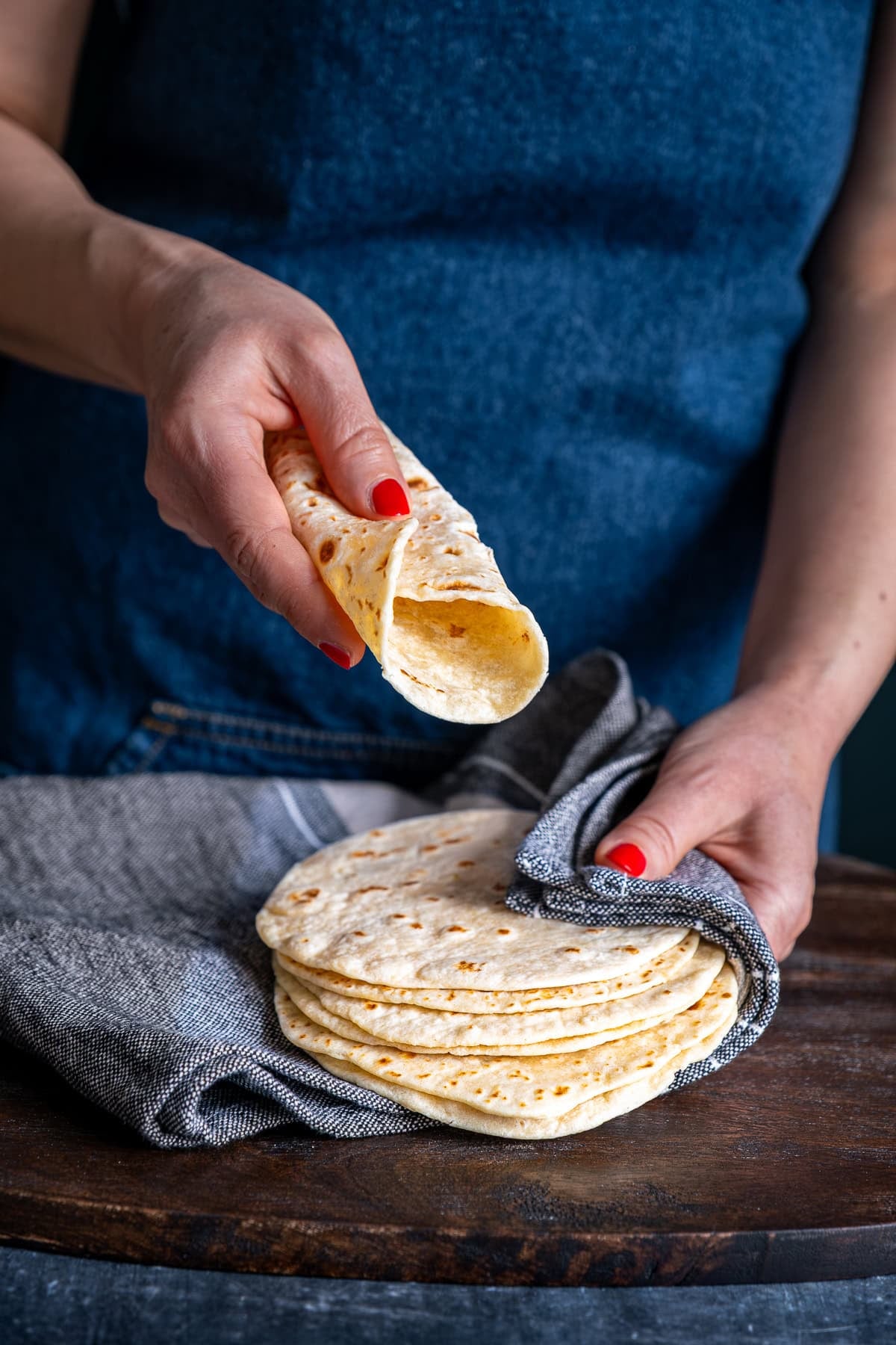 A pile of Easy Soft Flour Tortillas. One is rolled up and being held up to the camera.