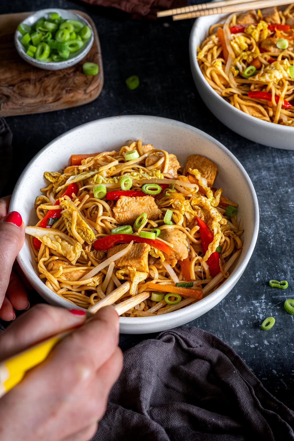 Easy Chicken Chow Mein in a bowl. A woman's hands are using chopsticks to take some out of the bowl.