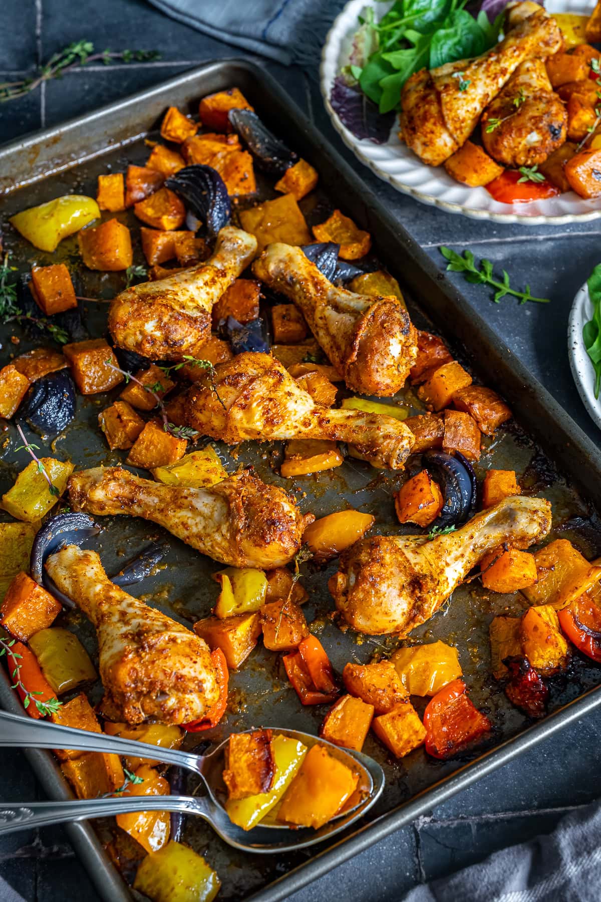 Chicken Drumstick Traybake in the tray with a plate of it behind the tray.