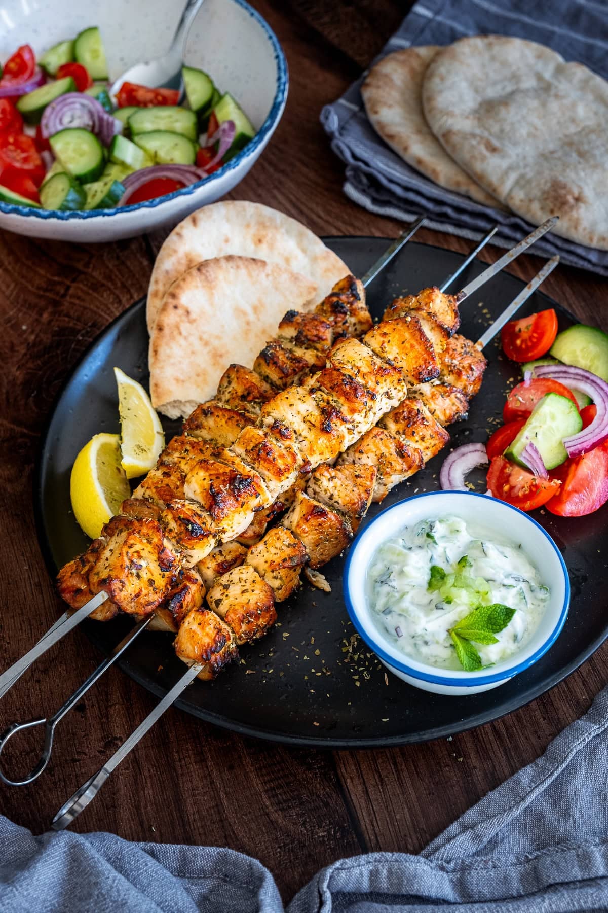 Chicken Kebabs on a plate with tzatziki, salad and pittas.