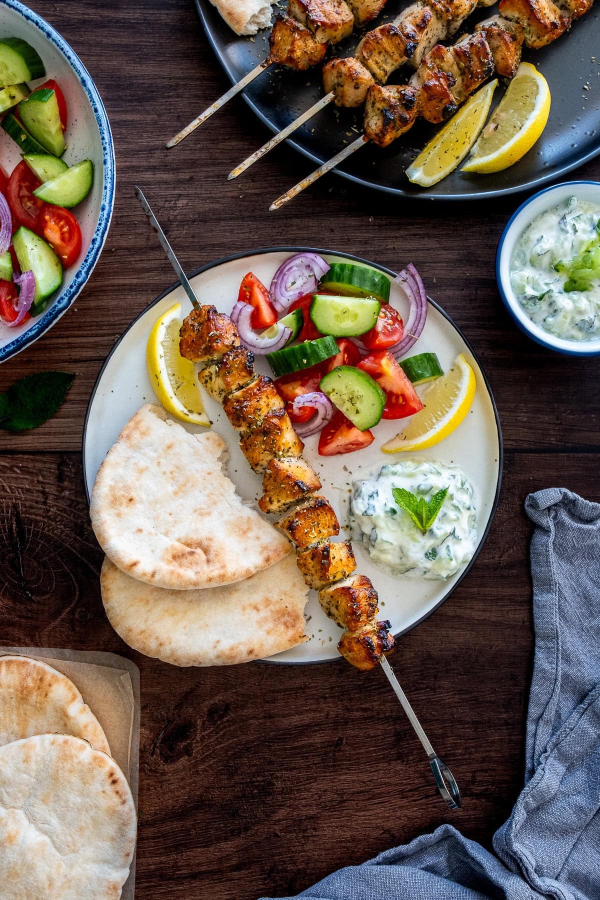 Overhead shot of 1 Greek chicken skewer on a plate with tzatziki, salad and pittas.