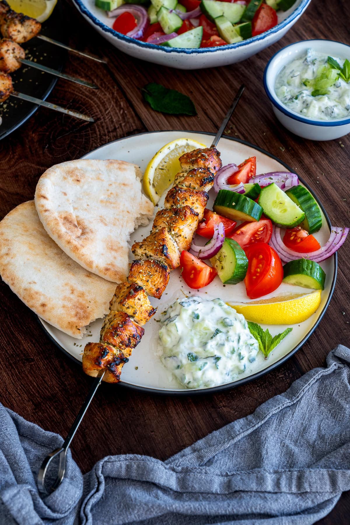 One chicken skewer on a plate with tzatziki, salad and pittas.
