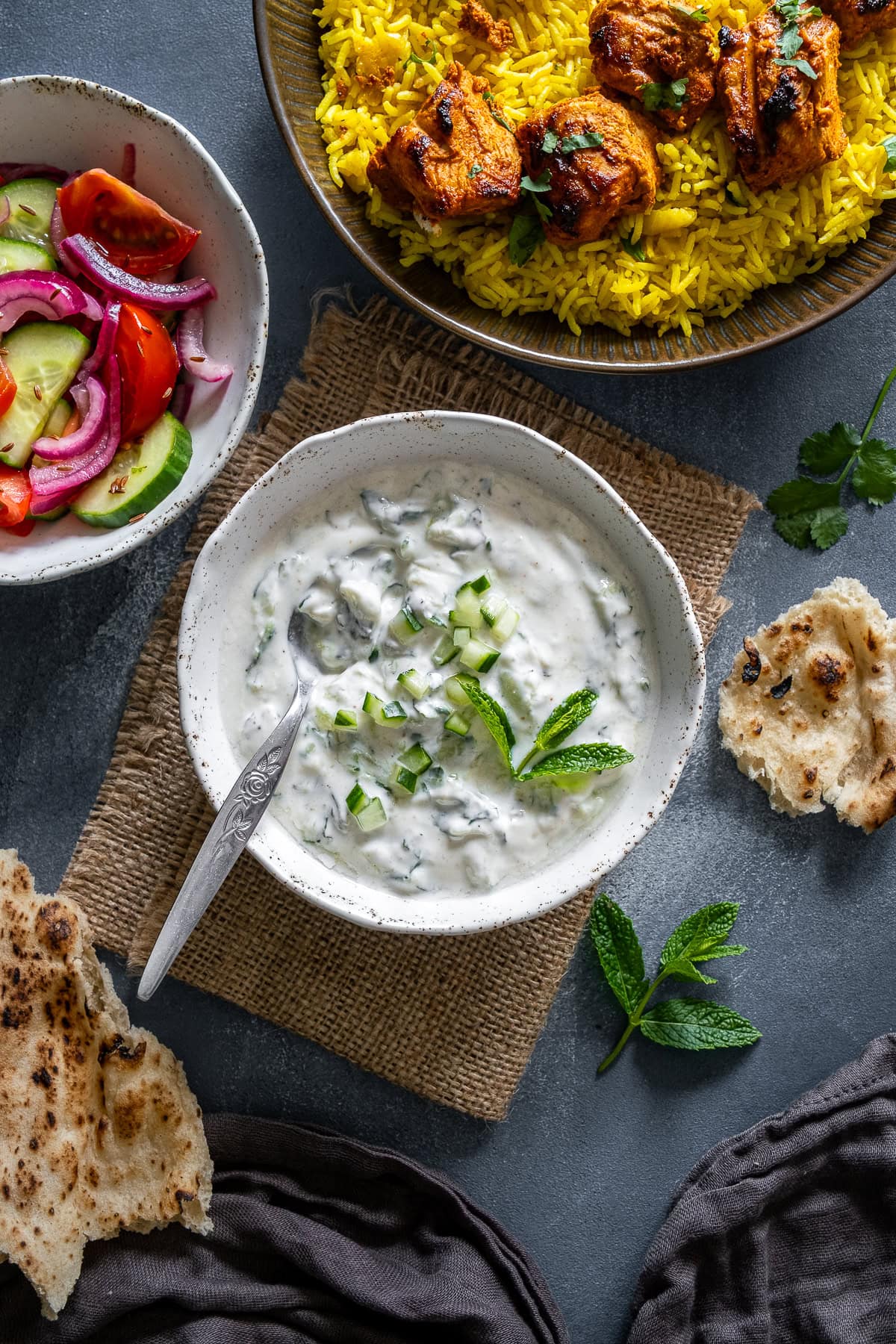 Overhead shot of Cucumber Mint Raita with Chicken Tikka Kebabs, Kachumber Salad and Pilau Rice.