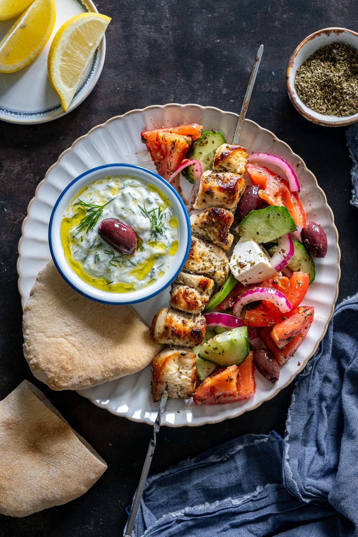 Overhead shot of Chicken Souvlaki on a plate with Greek Salad, Tzatziki and Pittas.