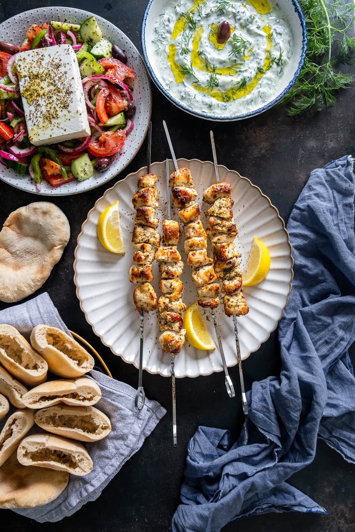 Overhead shot of Easy Chicken Souvlaki, surrounded by tzatziki, Greek salad and pitta bread.
