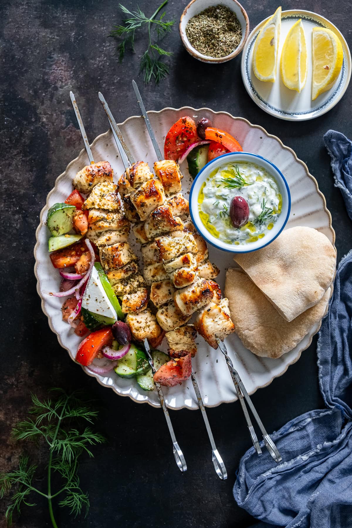 Overhead shot of Chicken Souvlaki on a plate with Greek Salad, Tzatziki and Pittas.