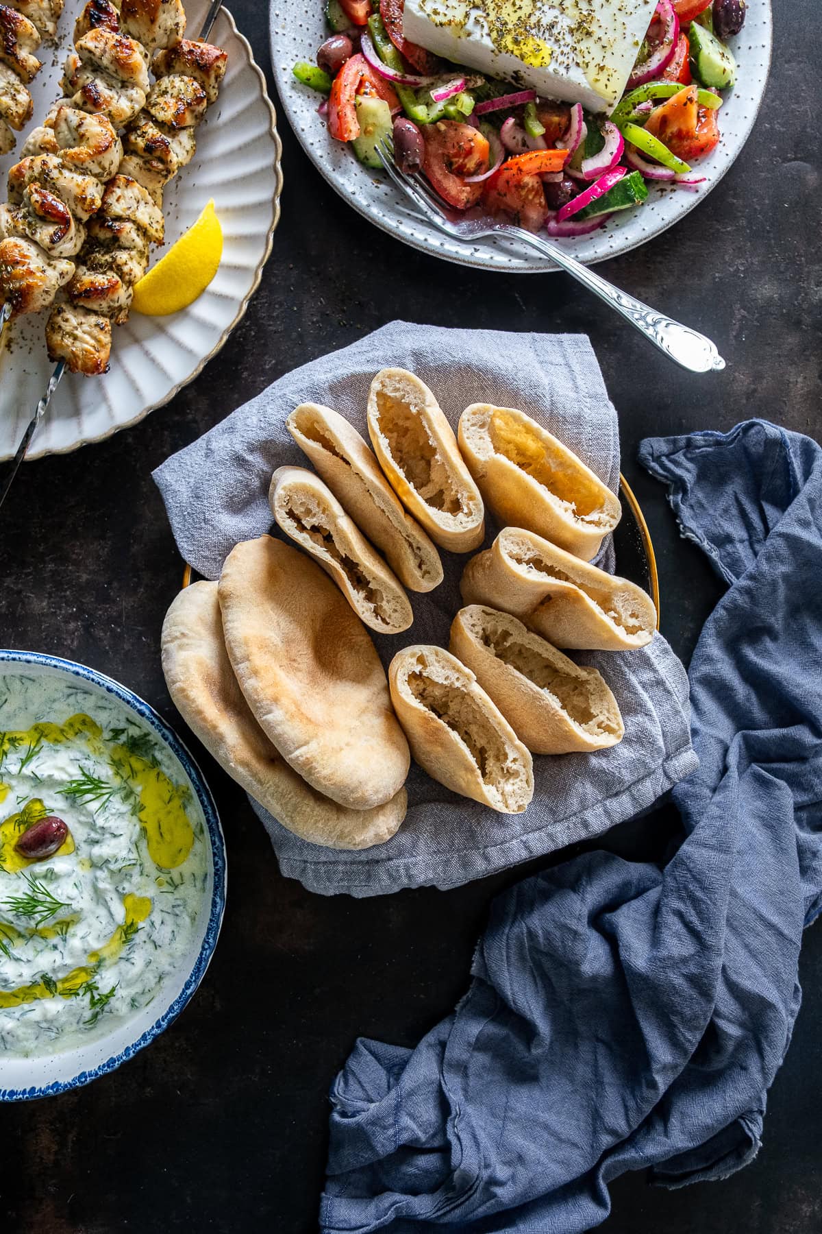 Overhead shot of Easy Homemade Pittas on a table with chicken souvlaki, greek salad and tzatziki.