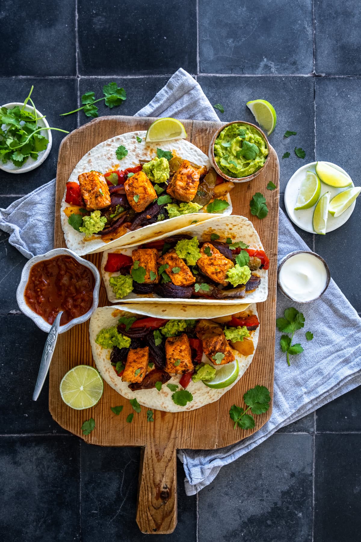 Overhead shot of 3 One Pan Salmon Fajitas on a board, surrounded by toppings.