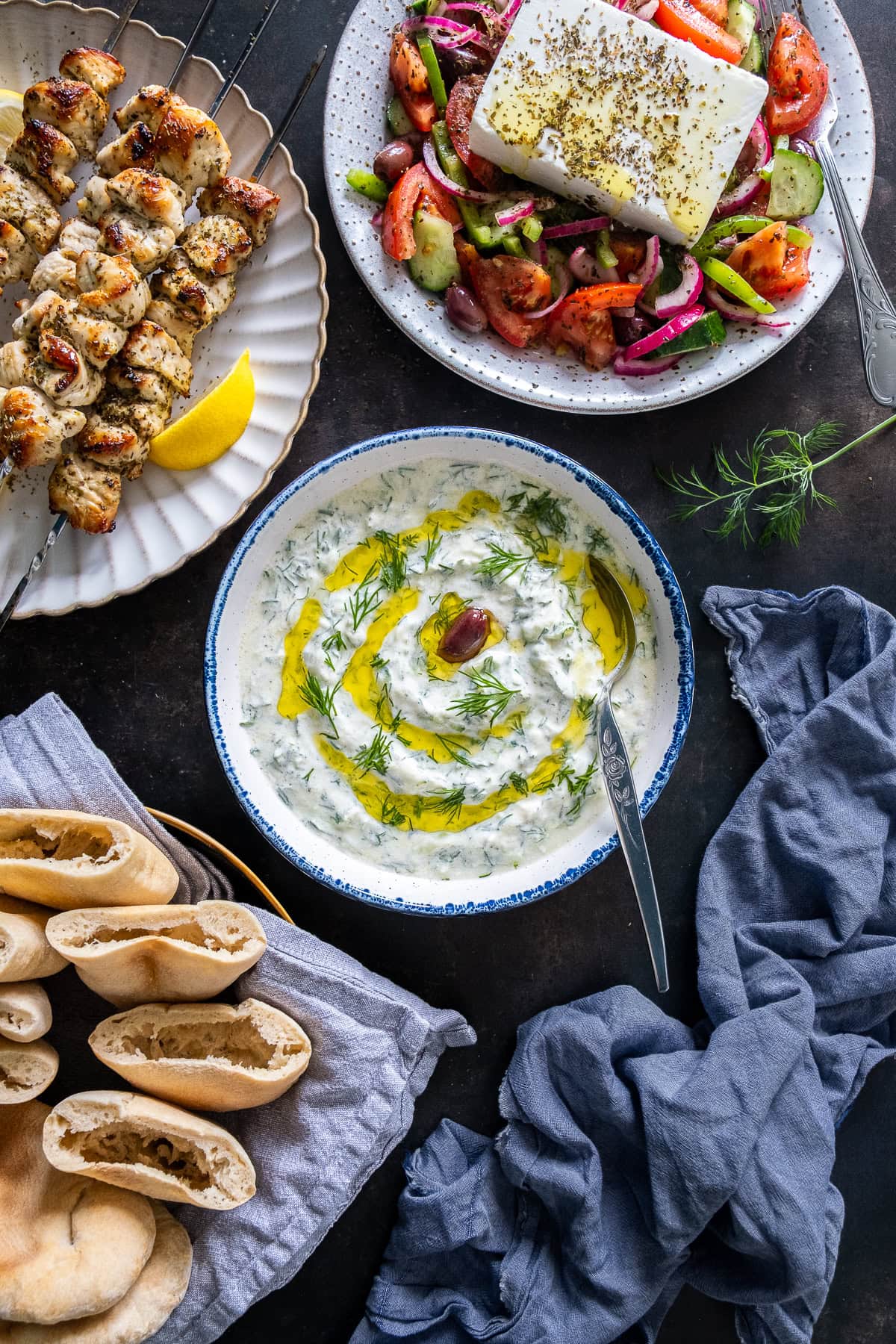 Authentic Greek Tzatziki, surrounded by Chicken souvlaki, greek salad and homemade pittas.