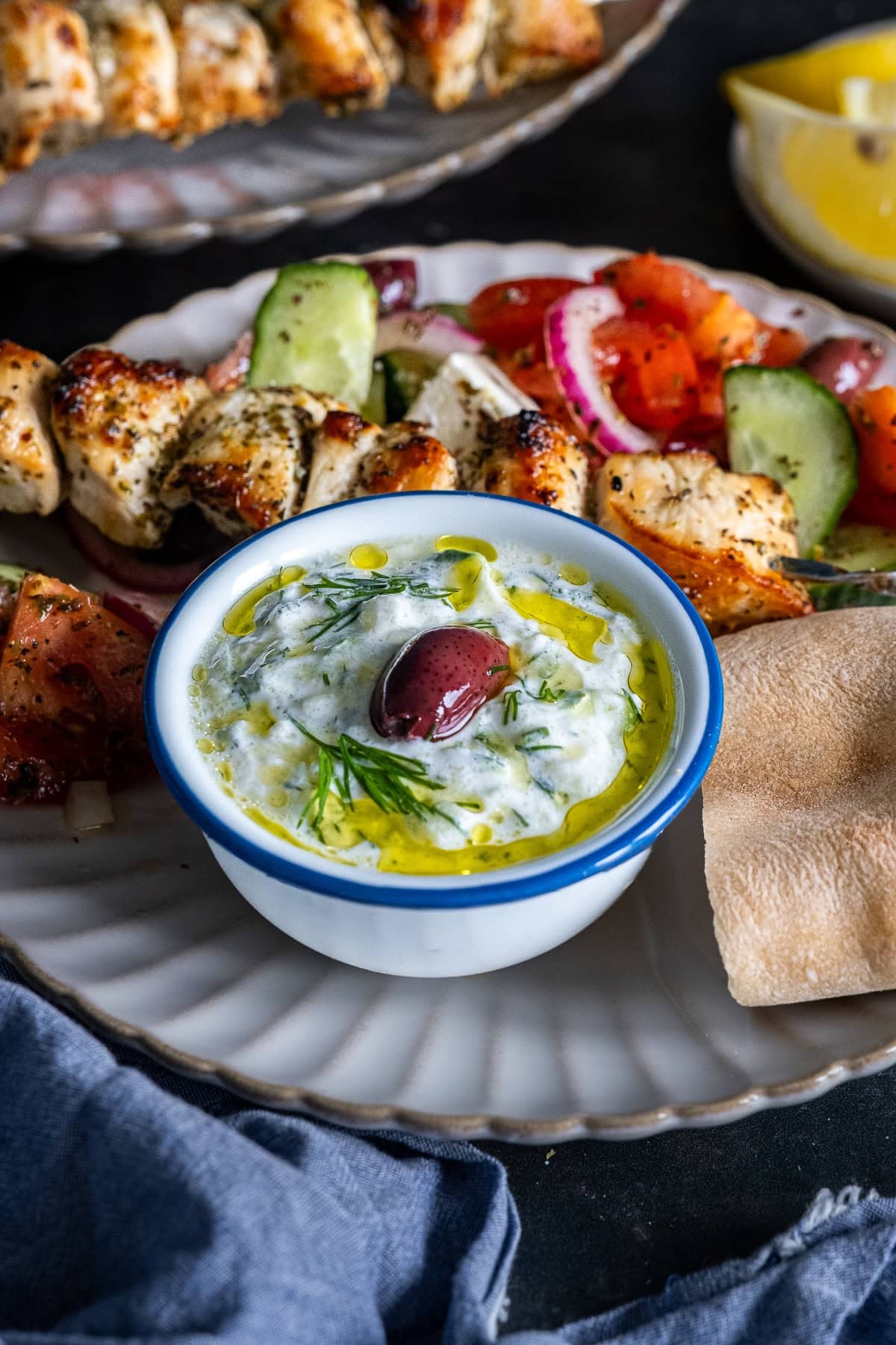 Closeup of Authentic Greek Tzatziki on a plate with Chicken souvlaki, greek salad and homemade pittas.