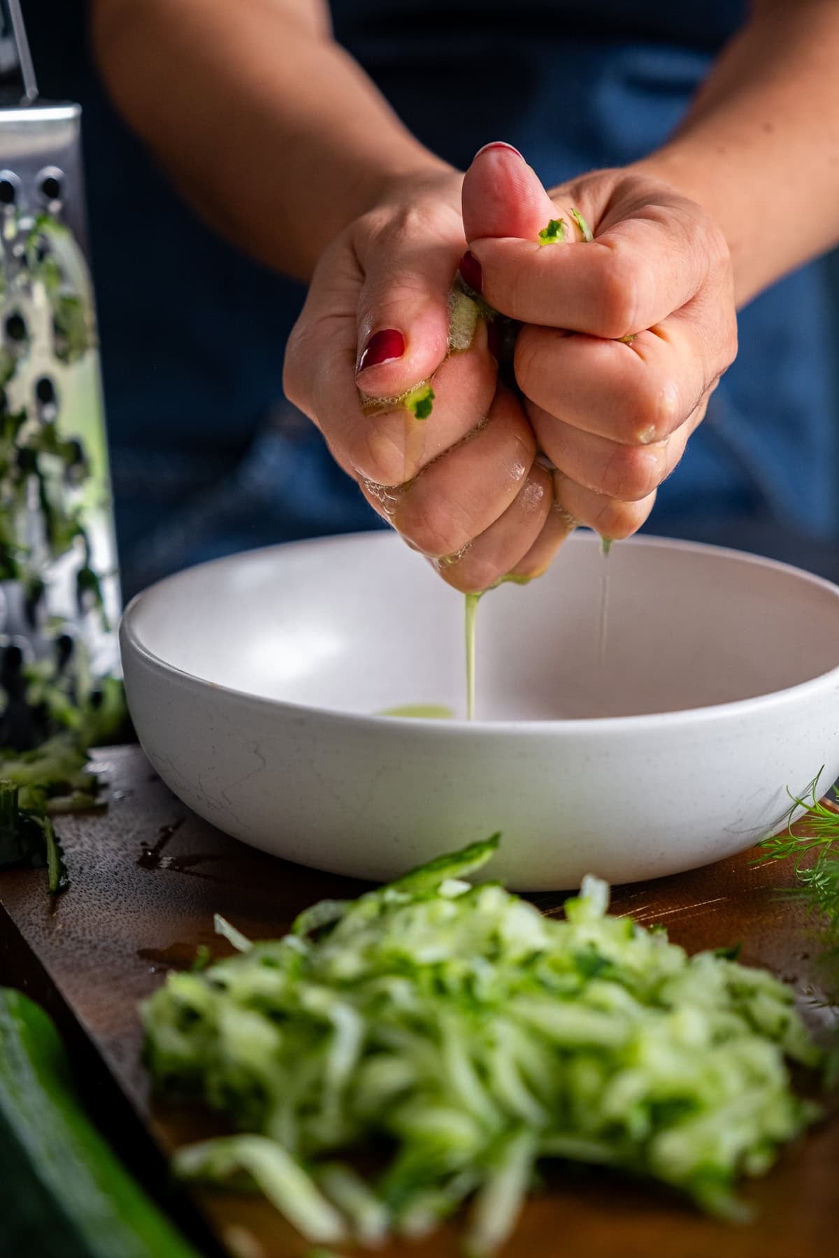 Woman's hands squeezing out cucumber for Authentic Greek Tzatziki
