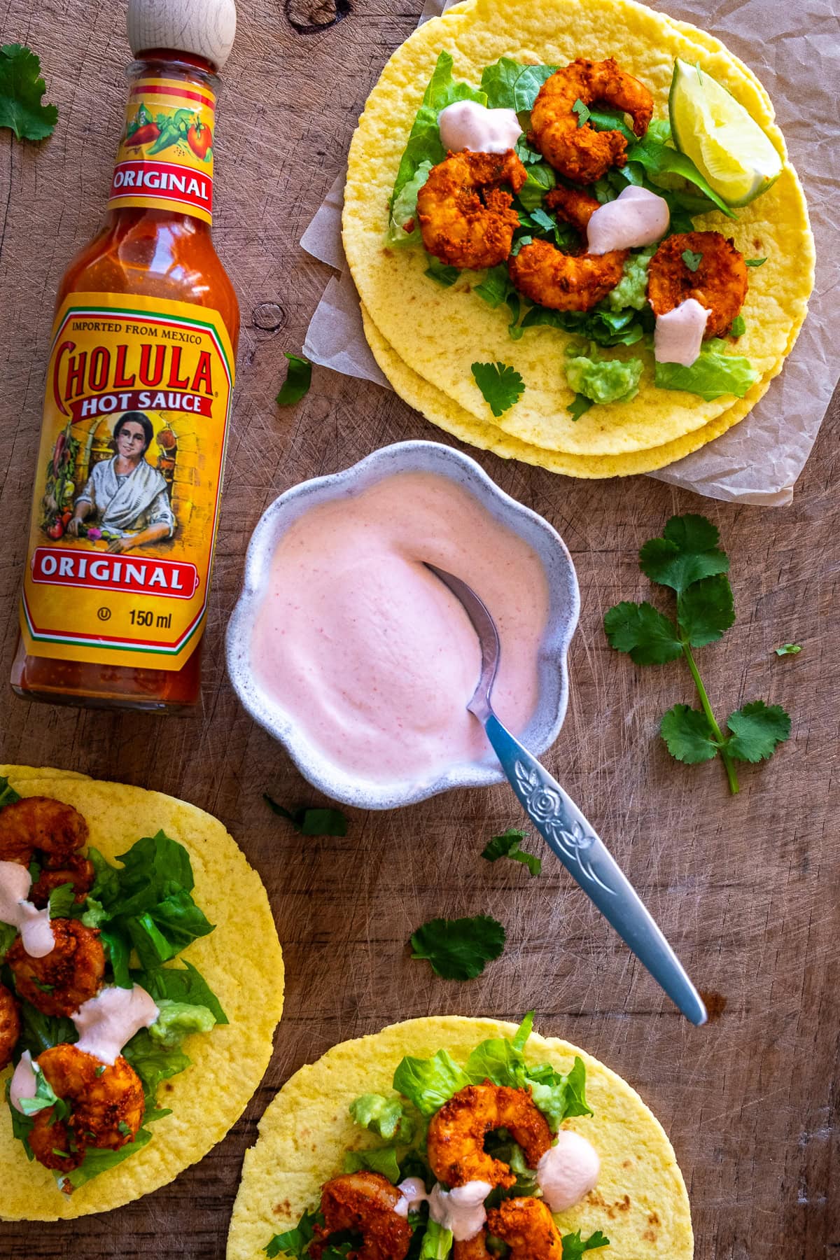 Overhead shot of Pink Taco Sauce in a bowl, surrounded by prawn tacos and bottle of Choula.