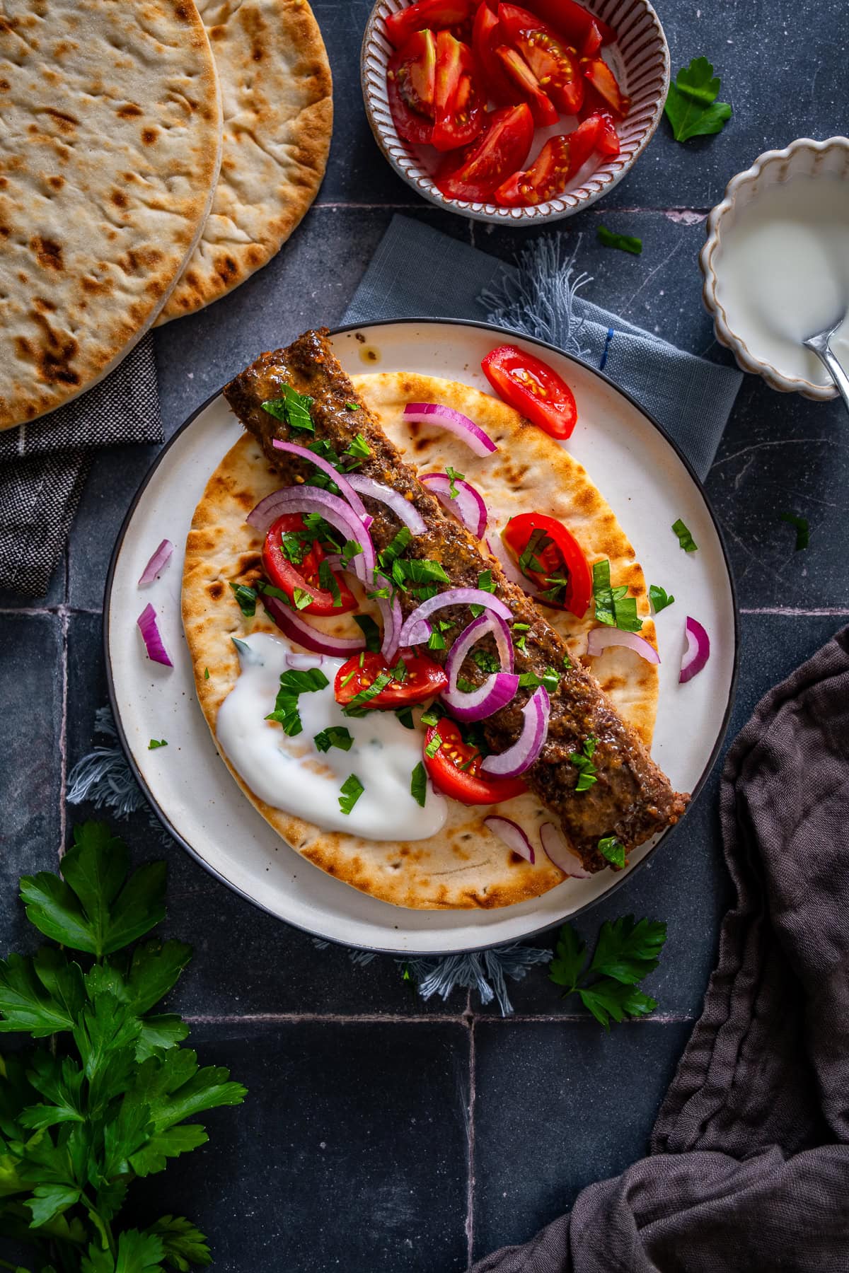 Overhead shot of one Sheet Pan Beef Kebab on a flatbread with yogurt, red onions and tomatoes.