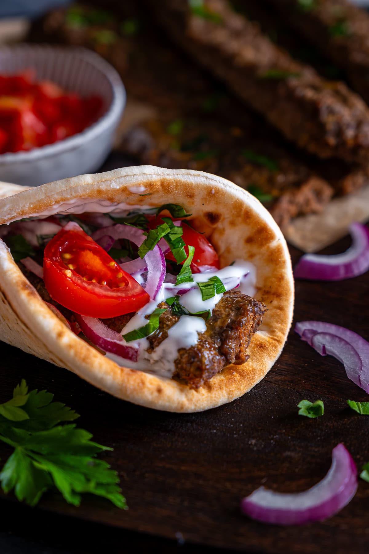 A Sheet Pan Beef Kebab inside a rolled up flatbread with yogurt, red onions and tomatoes.